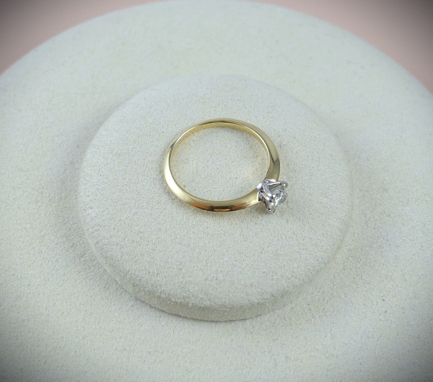 Der Ring 750 Gelbgold von Ninas Schmuckhandel mit einem 0,43 ct Brillanten in SI-Qualität in minimalistischer Krappenfassung wird elegant auf einem runden, hellbeigen Samtständer vor einem sanft verschwommenen, neutralen Hintergrund präsentiert. Ringgröße: 54.